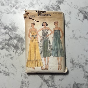 May include: Vintage Vogue Patterns envelope featuring illustrations of three different dresses. The dresses are strapless, with varying lengths and styles. The envelope is slightly torn and shows the Vogue Patterns logo and text.
