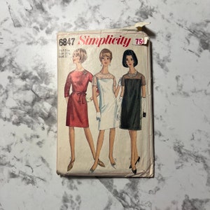 May include: Vintage Simplicity sewing pattern number 6847 size 16 1/2 bust 37. The pattern features three different dress designs: a red dress with a belt, a white dress with a lace neckline, and a black dress with a lace neckline. The pattern is in good condition and is ready to be used.