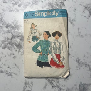 May include: Vintage Simplicity sewing pattern number 8117 for a blouse. The pattern is for size 12 miss and includes three different styles. The pattern cover features three women wearing the different blouse styles.