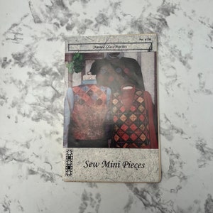 May include: A vintage sewing pattern for stained glass patches. The pattern features two vests with a diamond pattern in shades of red, blue, yellow, and brown. The text on the pattern reads "Stained Glass Patches" and "Sew Mini Pieces".