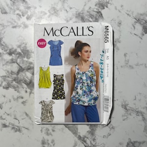 Puede incluir: Patrón de costura McCall's M6565 para tops. El sobre del patrón presenta ilustraciones de varios diseños de tops, incluyendo un top azul, un top amarillo, un top negro con lunares blancos y un top estampado. La palabra "EASY" está impresa en la parte delantera.