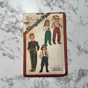 May include: Simplicity sewing pattern number 6048 for children's pants sizes 2, 3, 3, and 4. The pattern includes four different styles of pants, including a pair with suspenders.