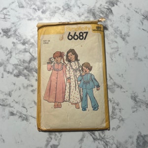May include: Simplicity sewing pattern number 6687 for children's pajamas. The pattern shows three girls wearing different styles of pajamas, including a pink gown, a floral print gown, and blue pajamas with a white trim.