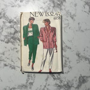 May include: A vintage New Look 6858 sewing pattern featuring illustrations of women's suits. One suit is green, and the other is a red and white striped blazer with white pants. The pattern is on a cream-colored background.