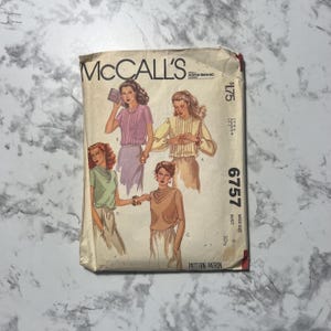 May include: Vintage McCall's sewing pattern, featuring illustrations of women's blouses. The pattern envelope is beige with the McCall's logo and the number 6757. The illustrations depict various blouse styles, including a cowl neck and pleated designs.