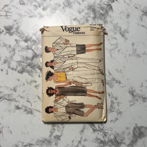 May include: A vintage Vogue Patterns sewing pattern envelope. The envelope features illustrations of women in various outfits, including blazers, skirts, shorts, and pants. The Vogue logo is at the top.