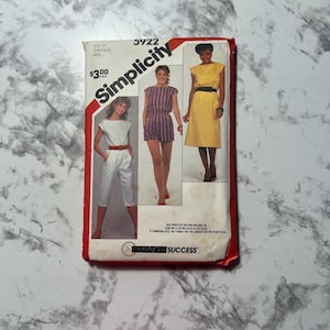May include: Simplicity sewing pattern number 5922 for a jumpsuit, shorts, and dress. The pattern is for sizes N (10-12-14) and M (16-18-20). The pattern costs £3.00. The pattern shows three different styles of clothing, all with short sleeves. The first style is a jumpsuit with a white top and white pants. The second style is a striped jumpsuit with a blue and white striped top and blue and white striped shorts. The third style is a yellow dress with a yellow top and a yellow skirt.