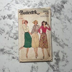 May include: Vintage sewing pattern for three skirts, featuring a green skirt with buttons, a cream skirt with a plaid pattern, and a floral print skirt. The pattern is from Butterick and is size 25. The pattern number is 5935.
