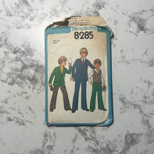 May include: Vintage Simplicity pattern 8285 for boys' clothing. The illustration shows three boys in different outfits: a green blazer with patterned pants, a blue suit, and a vest with green pants. The pattern is size 10.