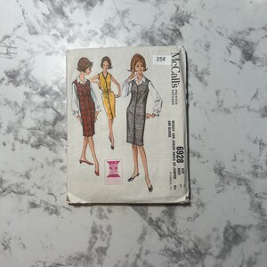 May include: A vintage McCall's sewing pattern for a dress or jumper with a blouse. The pattern is for misses and juniors, sizes 14, 34, and 65. The pattern is printed on a white background with a black and white illustration of a woman wearing the dress.