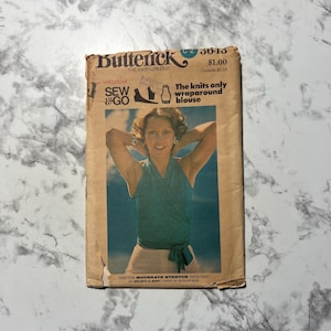 May include: A vintage Butterick sewing pattern, featuring a woman wearing a teal wraparound blouse. The pattern cover includes the text "SEW & GO" and "The knits only wraparound blouse". The pattern is sized for moderate stretch knits.