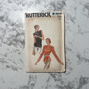 May include: Vintage Butterick sewing pattern 6910, size 12. The pattern features illustrations of two different blouses. The cover is off-white with the Butterick logo and text in black. The illustrations show a black top and an orange top.