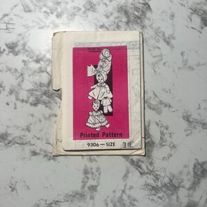 May include: A vintage sewing pattern for a doll's wardrobe. The pattern is printed on pink paper and features illustrations of dolls wearing different outfits. The pattern number is 9306.