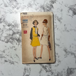 May include: Vintage Vogue pattern envelope featuring illustrations of two women in 1960s dresses. The envelope is tan with the text "Vogue Pattern" and the price $1.50. The illustrations depict a yellow dress with black sleeves and a white dress.