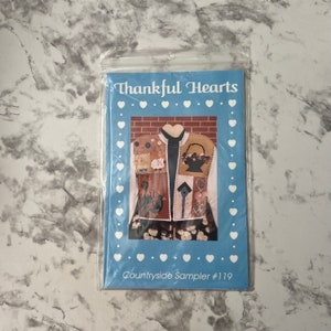 May include: A blue and white printed paper pattern for a quilted vest with the title "Thankful Hearts" and "Countryside Sampler #119". The vest is pictured in the center of the pattern and features a variety of patchwork designs.