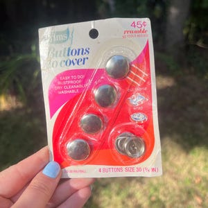 May include: A package of silver-colored buttons, size 30 (¾ in), for covering. The package is red and white with the text "Buttons to cover", "Easy to do, rustproof, dry cleanable, washable", and "45¢ reusable".