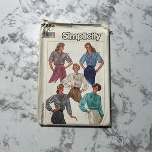 Puede incluir: Un patrón de costura Simplicity vintage, blanco con el logotipo de Simplicity y el número 7854. Las ilustraciones muestran varios diseños de blusas con diferentes largos de manga y colores. El patrón es para blusas.