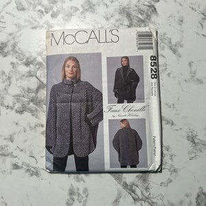 Puede incluir: Sobre de patrón de costura McCall's para un abrigo de imitación de chenilla. El número de patrón es 8528. El sobre muestra a una modelo con un abrigo gris y blanco con cuello negro y un botón negro.