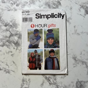 May include: Simplicity sewing pattern number 9749 for making hats and scarves. The pattern includes instructions for making a variety of styles, including a blue and white striped hat, a red and white striped hat, a blue and white striped scarf, and a red and white striped scarf.