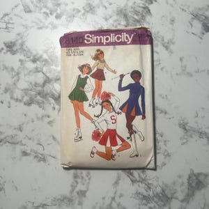May include: Vintage Simplicity sewing pattern 8140. The pattern envelope shows illustrations of young girls in skating and cheerleading outfits. The envelope is purple and white with the Simplicity logo and pattern number.