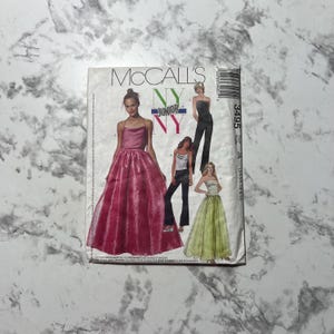 May include: McCall's sewing pattern for a dress, featuring three different styles. The pattern number is 3495 and the size is Junior. The dress is pink, green, and black.