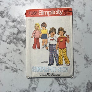 May include: Simplicity sewing pattern number 7061 for toddlers. The pattern includes instructions for making a variety of clothing items, including pants, shirts, and tops. The pattern is designed for stretch knits only. The pattern cover features illustrations of four children wearing the clothing items.