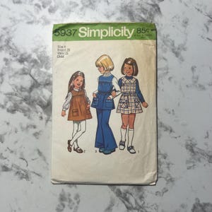 May include: Vintage Simplicity sewing pattern number 5937 for a child's dress. The pattern includes three different styles: a brown dress with pockets, a blue jumpsuit with a bib, and a plaid dress with a Peter Pan collar. The pattern is for size 4, with a 23 inch bust and 21 inch waist.