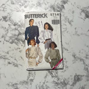 May include: A Butterick sewing pattern packet featuring illustrations of women's blouses. The packet has the number 5714 and includes the size range 12-14-16. The cover shows four different blouse designs in various colors and styles.