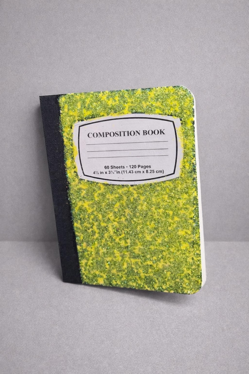 May include: A composition book with a yellow and green glitter design. The cover has a white label that reads "COMPOSITION BOOK". The notebook measures 11.43 cm x 8.25 cm.