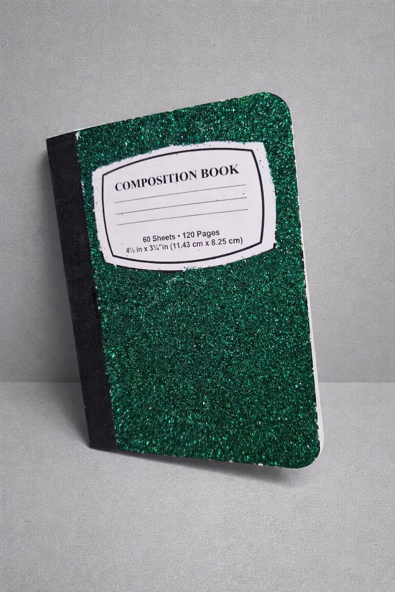 May include: A green glitter composition book with a black spine. The cover features a white label with the words "COMPOSITION BOOK" and details: 60 sheets, 120 pages, and dimensions of 4.5 in x 3.25 in.