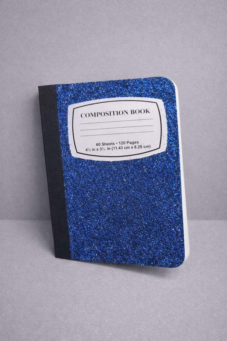 Op de afbeelding: Een blauw glitter compositieboek met een zwarte rug. De kaft heeft een wit label met de tekst "COMPOSITION BOOK". Het notitieboek meet 11,43 cm x 8,25 cm.