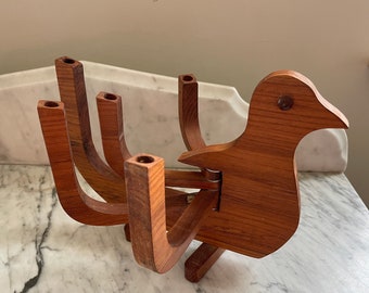May include: A wooden candle holder in the shape of a bird. The bird has a long neck and a beak. The candle holder has five openings for candles. The wood is a warm brown color.
