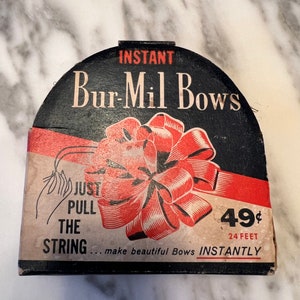 May include: Vintage Bur-Mil Bows dispenser. The black and red packaging features the text "INSTANT Bur-Mil Bows" and a graphic of a red bow. The packaging also includes the text "JUST PULL THE STRING" and "24 FEET".