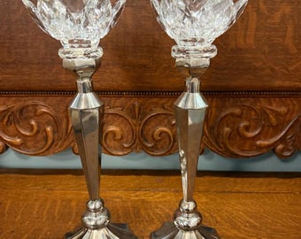 May include: Two silver candlesticks with crystal lotus flower-shaped tops. The candlesticks have a faceted, tapered stem and a multi-sided base. The crystal tops are clear and reflect light, adding a touch of elegance to the design.