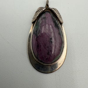 May include: A silver pendant with a large, teardrop-shaped stone. The stone is a mix of deep pink and green hues, set in a silver frame. Two leaf-shaped accents sit at the top of the pendant.