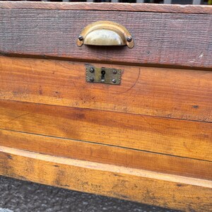 Puede incluir: Primer plano de un cofre de madera vintage con un asa y cerradura de lat&oacute;n. El cofre est&aacute; hecho de madera te&ntilde;ida con vetas visibles y una parte superior oscura. La ferreter&iacute;a tiene un aspecto deslustrado.
