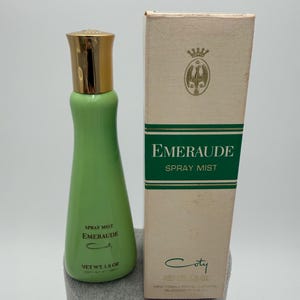 May include: A light green bottle of Emeraude Spray Mist with a gold cap, labeled Net Wt. 1.8 oz, alongside its matching rectangular box. The box features a gold crest, the text Emeraude Spray Mist, and the Coty brand name in dark green ink.