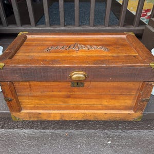 Puede incluir: Un ba&uacute;l de madera vintage con herrajes de lat&oacute;n. El ba&uacute;l tiene forma rectangular con un dise&ntilde;o tallado en la tapa. La madera tiene un tono marr&oacute;n rojizo c&aacute;lido. El ba&uacute;l mide aproximadamente 76 cm de ancho, 46 cm de profundidad y 51 cm de alto.