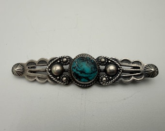 Puede incluir: Horquilla plateada para el cabello con una piedra de turquesa central. La horquilla presenta elementos decorativos que incluyen detalles en forma de cuerda, cuentas plateadas y bordes festoneados. La horquilla mide aproximadamente 10 cm de largo.