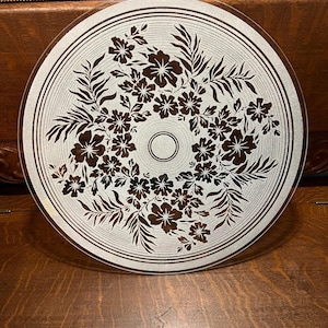 May include: A round, clear glass ceiling light cover with a floral design. The design features brown flowers and leaves arranged in a circular pattern. The cover has concentric rings around the edge and a central circle.
