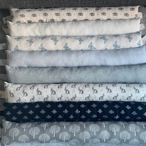 May include: A set of ten doorstops in various patterns. The doorstops are made of a soft, fabric material and feature different designs, including butterflies, rabbits, and geometric patterns. The doorstops are all in shades of grey and black.