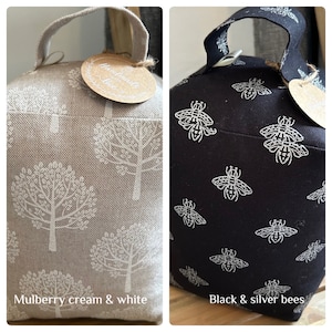 May include: Two doorstop cushions. One is cream with a white tree pattern and the text "Handmade with Love". The other is black with a silver bee pattern. Both have a loop handle.