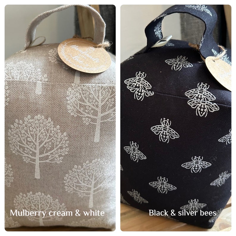 May include: Two doorstop cushions. One is cream with a white tree pattern and the text "Handmade with Love". The other is black with a silver bee pattern. Both have a loop handle.
