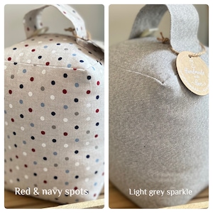 May include: Two doorstops, one with a light gray sparkle finish and the other with a beige fabric with red and navy blue polka dots. Both doorstops have a fabric handle and a tag that says "Handmade with Love".