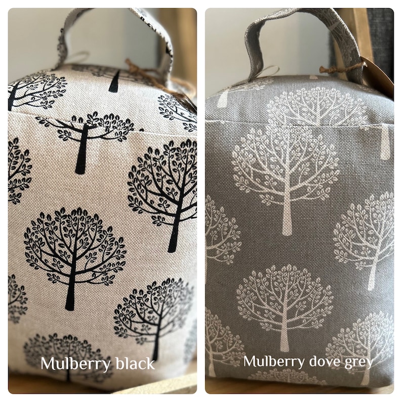 May include: Two doorstops with a tree pattern. The doorstop on the left is beige with black trees. The doorstop on the right is gray with white trees. The doorstop on the left is labeled "Mulberry black" and the doorstop on the right is labeled "Mulberry dove grey".