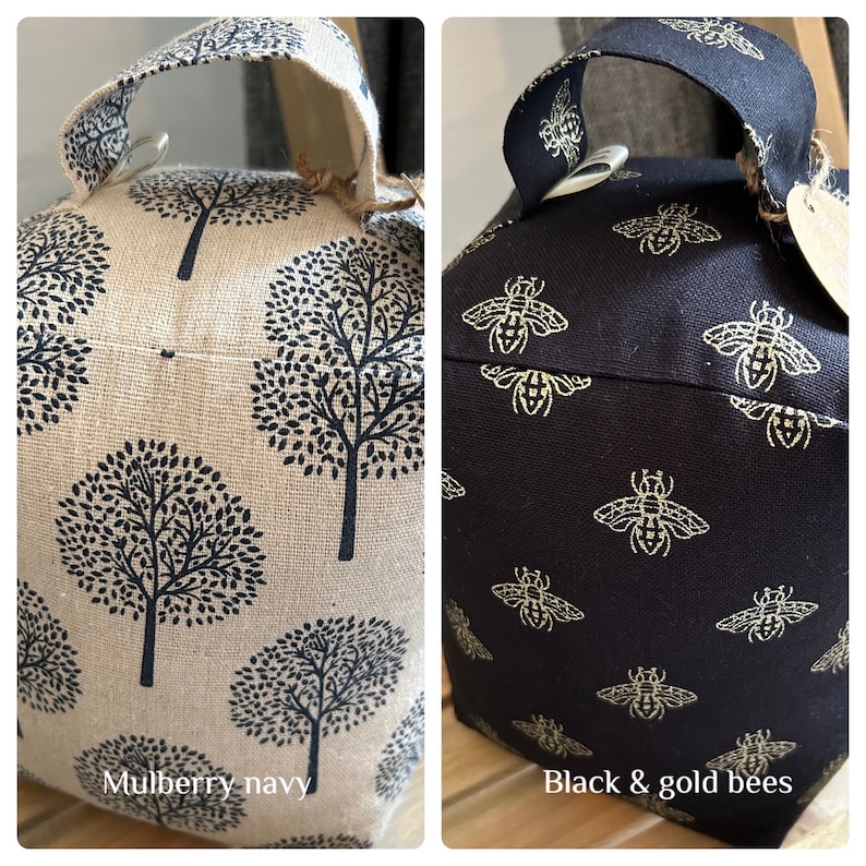 May include: Two doorstop cushions. One is beige with a black tree pattern and the text "Mulberry-navy". The other is black with a gold bee pattern and the text "Black & gold bees".