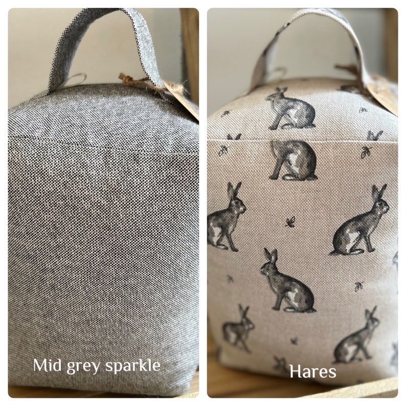 May include: Two doorstop cushions. One is a solid mid-grey color with a sparkle finish. The other is a beige fabric with a repeating pattern of black hares. The text "Hares" is printed below the cushion.