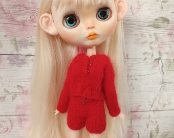 Puede incluir: Una muñeca con el pelo largo y rubio que lleva un conjunto de jersey y pantalones cortos de punto rojo. La muñeca tiene ojos azules y una cara pintada.