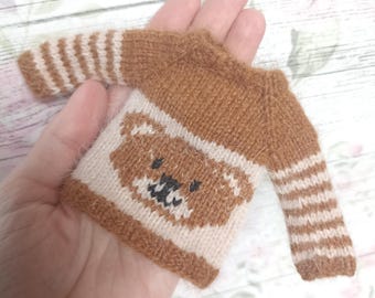 May include: A brown knitted sweater with a white bear design on the front and brown and white striped sleeves.