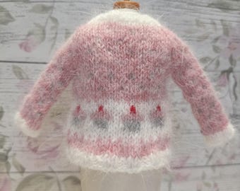 May include: A miniature pink and white knitted sweater with long sleeves. The sweater features a white collar and cuffs, with a pattern of gray and red floral designs on the lower portion. The garment is displayed on a small mannequin.
